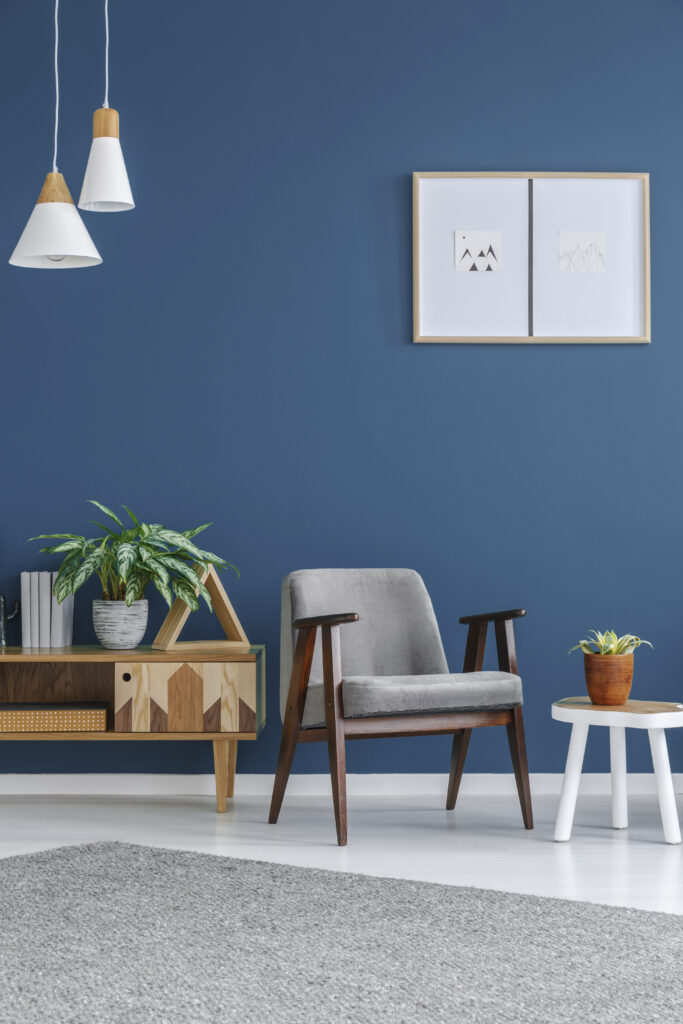 Modern grey armchair, wooden cabinet and plant in blue room