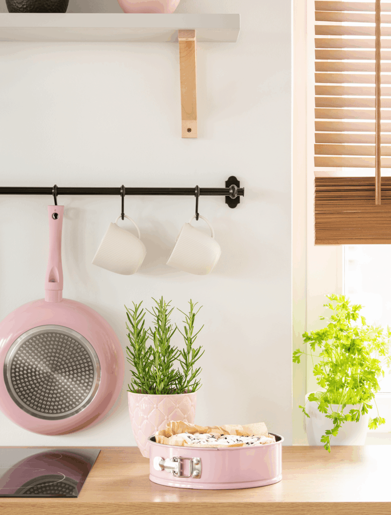 Pink baking pan with tart on wooden counter, rosemary, and mugs hanging.