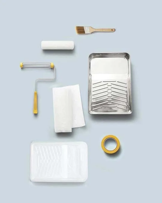 Paint roller, brush, trays, tape and cloths on a blue background
